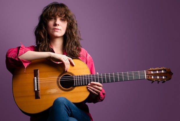Guitarist Laura Snowden holding instrument  while sitting against a purple background.