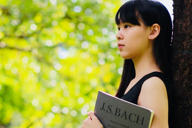Pianist Min Duh leaning against a tree holding Bach score