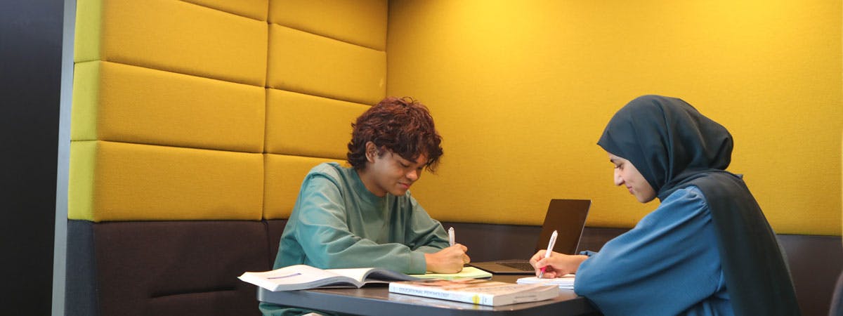 Two students writing on notepads in study booth