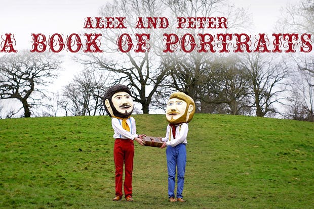 Two men in a field wearing giant papier maché heads. Plus text: "A Book of Portraits"