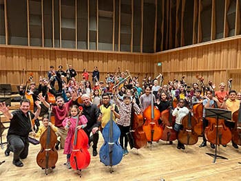 Children posing with mini-basses on the Bradshaw Hall Stage with Tony Alcock and Claus Freudenstein