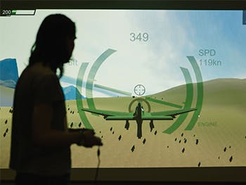 Photograph of CGT student playing game on controller, in front of a projector screen