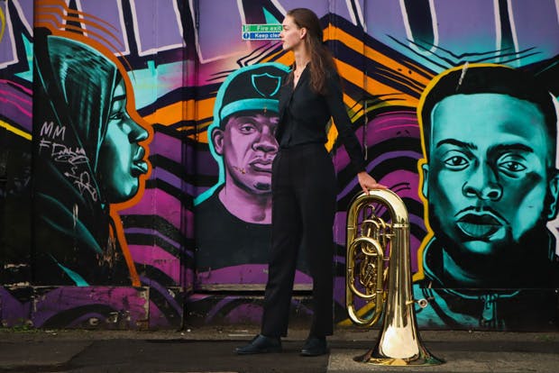 Tuba player standing in profile in front of graffiti-ed wall