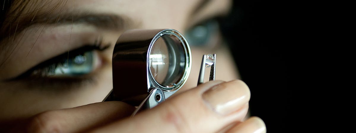 Student holding a Dimond up with tweezers and looking at it through a loupe. 