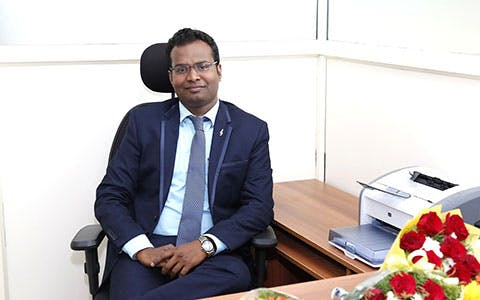 Dr A R Renukaprasad sitting at a desk.