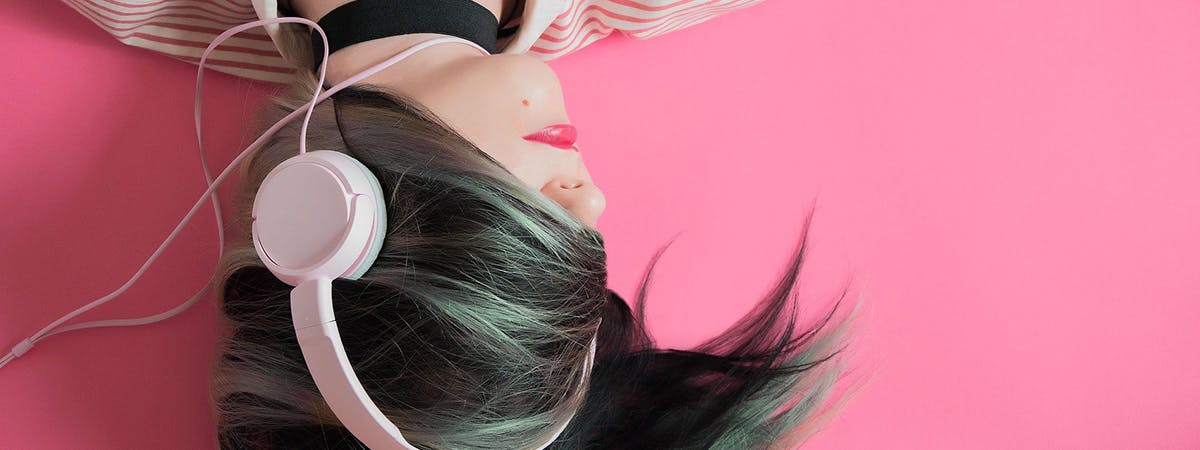 Girl lying on pink background wearing headphones