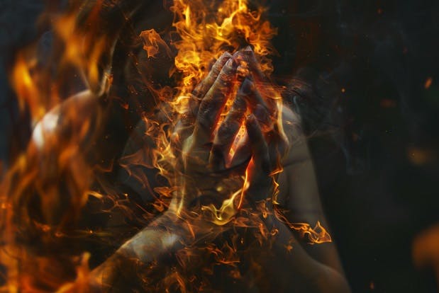 A woman's hands clasped in prayer, engulfed in flames