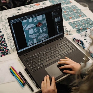 Student at laptop working on fabric design patterned with colourful mushrooms
