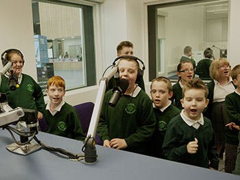 Children recording a podcast around the microphones in Birmingham City University's radio studios
