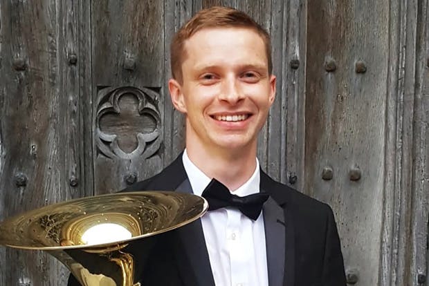 Alexander Hucknall in formal wear cradling French horn
