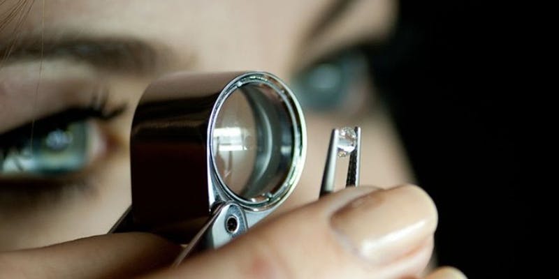 Woman examining gemstone through magnifier