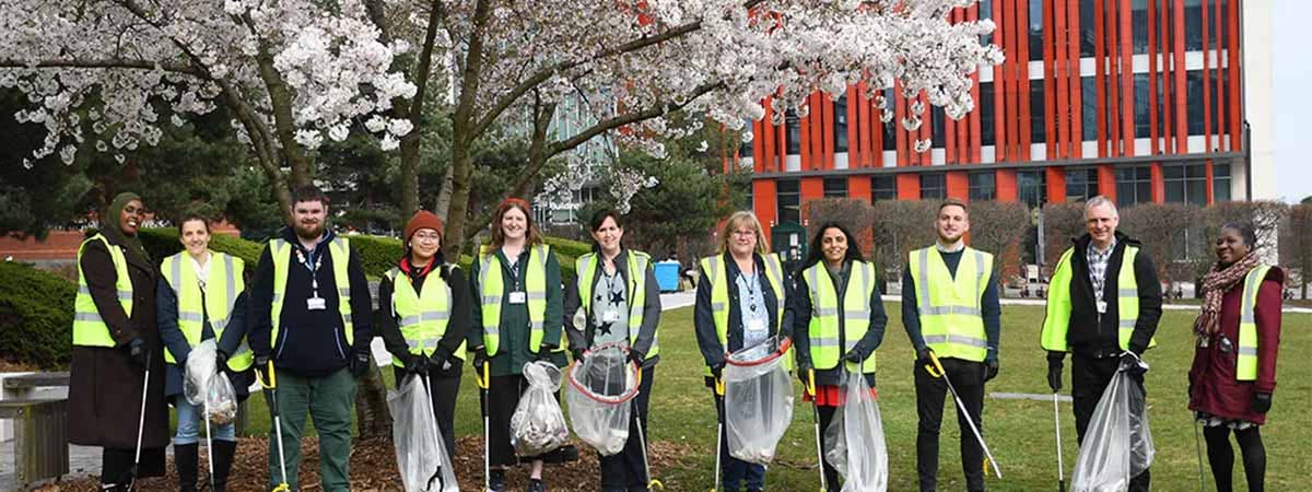 A group of people wearing hi-vis with litter picking equipment smiling