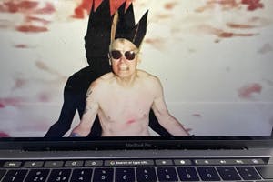 Naked man wearing paper crown and sunglasses shouting out from laptop screen