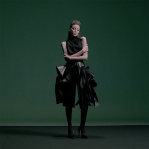 A woman in a black skirt standing in front of a green screen.