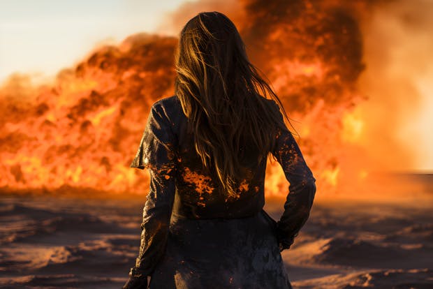 Young woman with back to viewer stands observing an oil fire