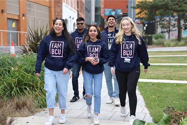 A group of 5 students walking through campus wearing hoodies saying I AM BCU on them. 
