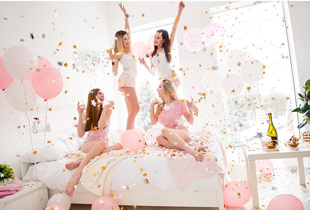 Four girls jumping on bed in pink bedroom with balloons and confetti