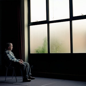 Photography piece of person sitting on a chair looking out of a large window