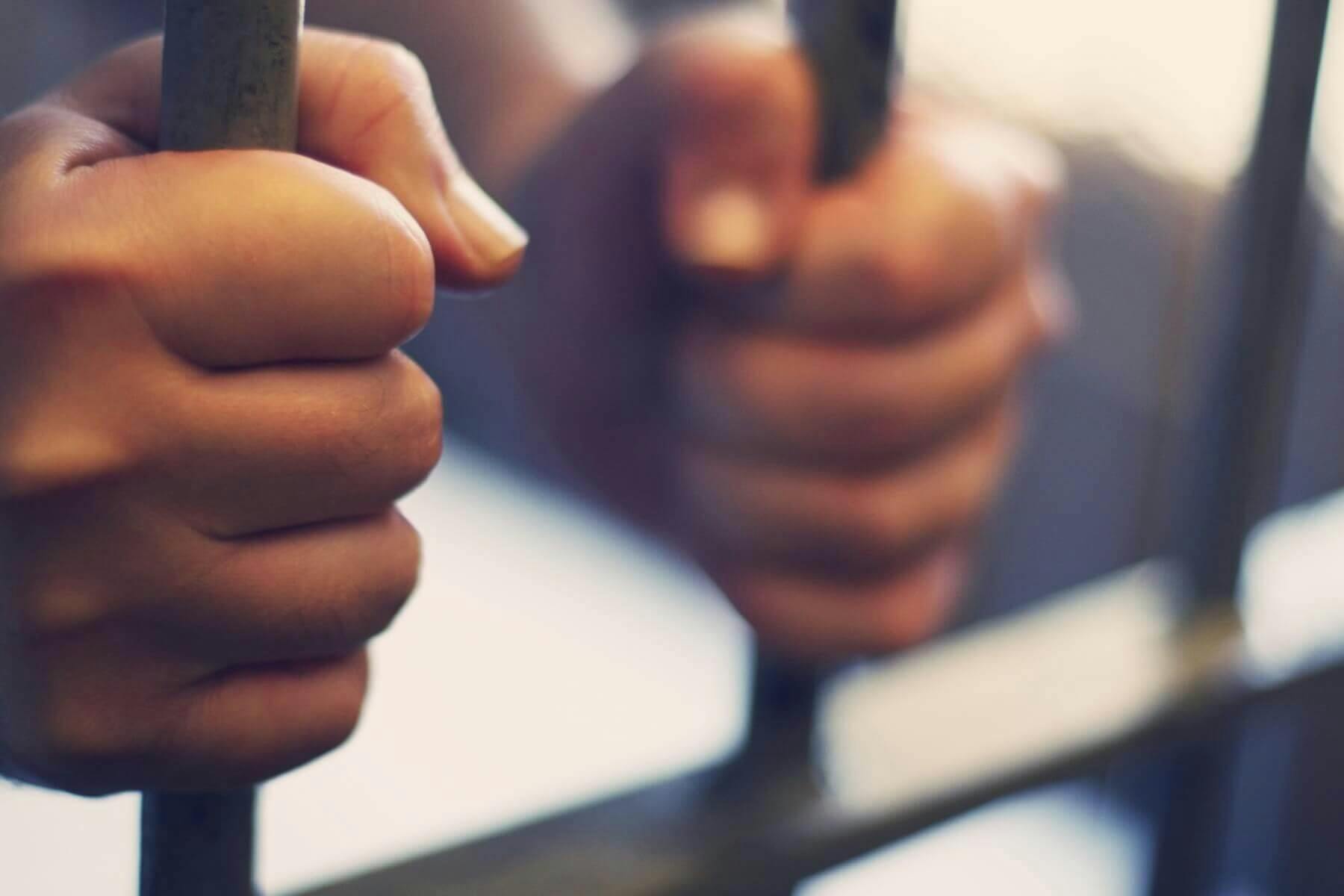 A pair of hands holding the bars of a prison cell