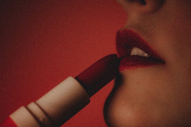 Profile close-up, woman applying lipstick, red background