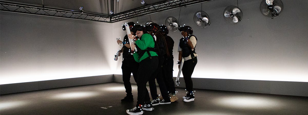 A group of students in a VR experience looking scared. They're holding plastic guns and have colourful sensors on their wrists and ankles