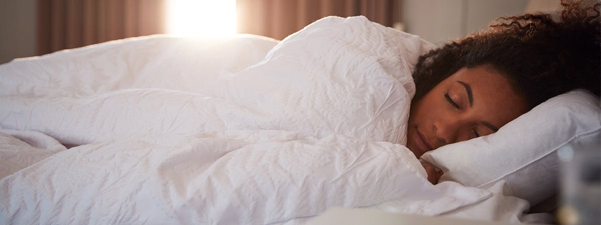 a woman sleeping in a bed with a white duvet and pillow