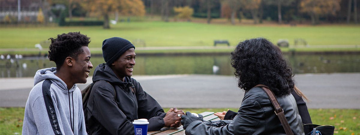 Students sitting at a picnic table in Cannon Hill park talking and laughing