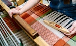 Student at weaving loom creating complex fabric design in red, white, green and blue
