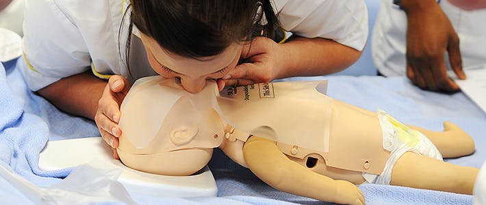 BCU Health Child Nursing student practicing mouth to mouth on a child dummy.