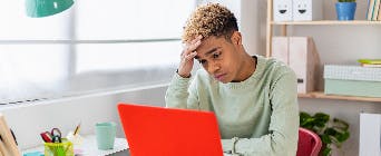 Person looking at a laptop looking concerned with head in hand