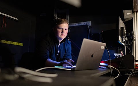 Will - stage management student - sitting backstage with a laptop